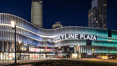 Das Einkaufszentrum Skyline Plaza bei Nacht mit erleuchteter Schrift und moderner Außenfassade.