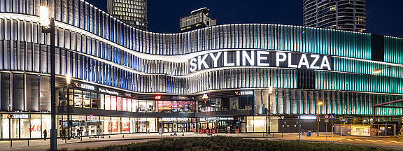 Das Einkaufszentrum Skyline Plaza bei Nacht mit erleuchteter Schrift und moderner Außenfassade.