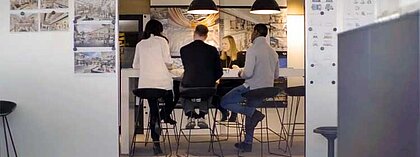Mehrere Mitarbeiter und Mitarbeiterinnen eines Design-Büros sitzen gemeinsam an einem Tisch