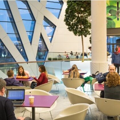 Mehrere Personen sitzen an Tischen in einem Gastronomiebereich eines Shopping-Centers.