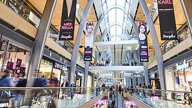 Einige Werbeplakate hängen von der Decke eines gut besuchten Shopping-Centers