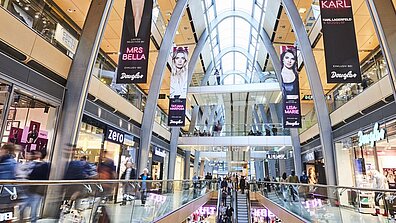 Einige Werbeplakate hängen von der Decke eines gut besuchten Shopping-Centers
