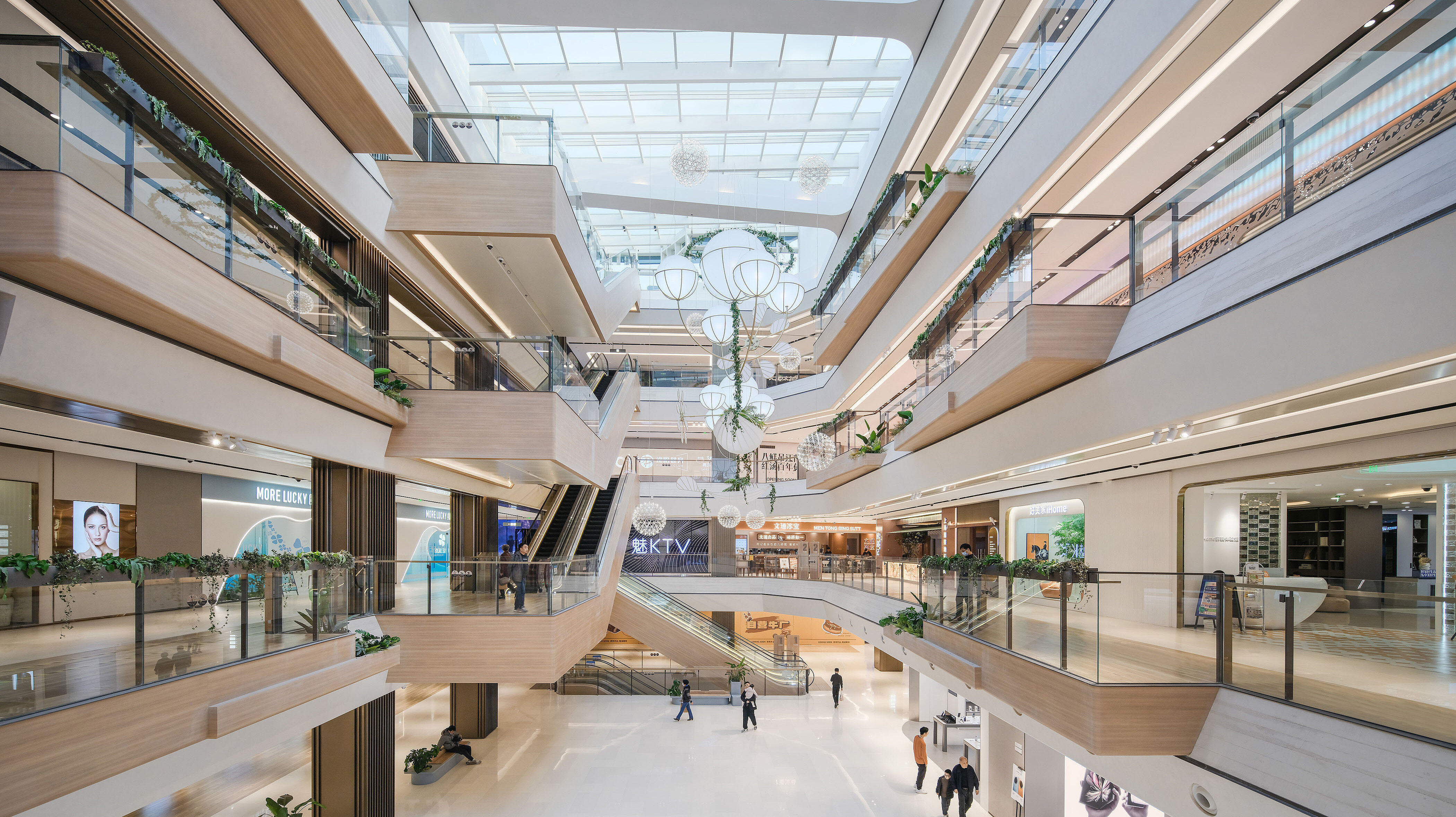 Blick ins Innere eines in hellen Farben gehaltenen Shopping-Centers mit architektonischen Besonderheiten, heller Holzverkleidung und Sonnenlicht, das durch das Glasdach fällt.
