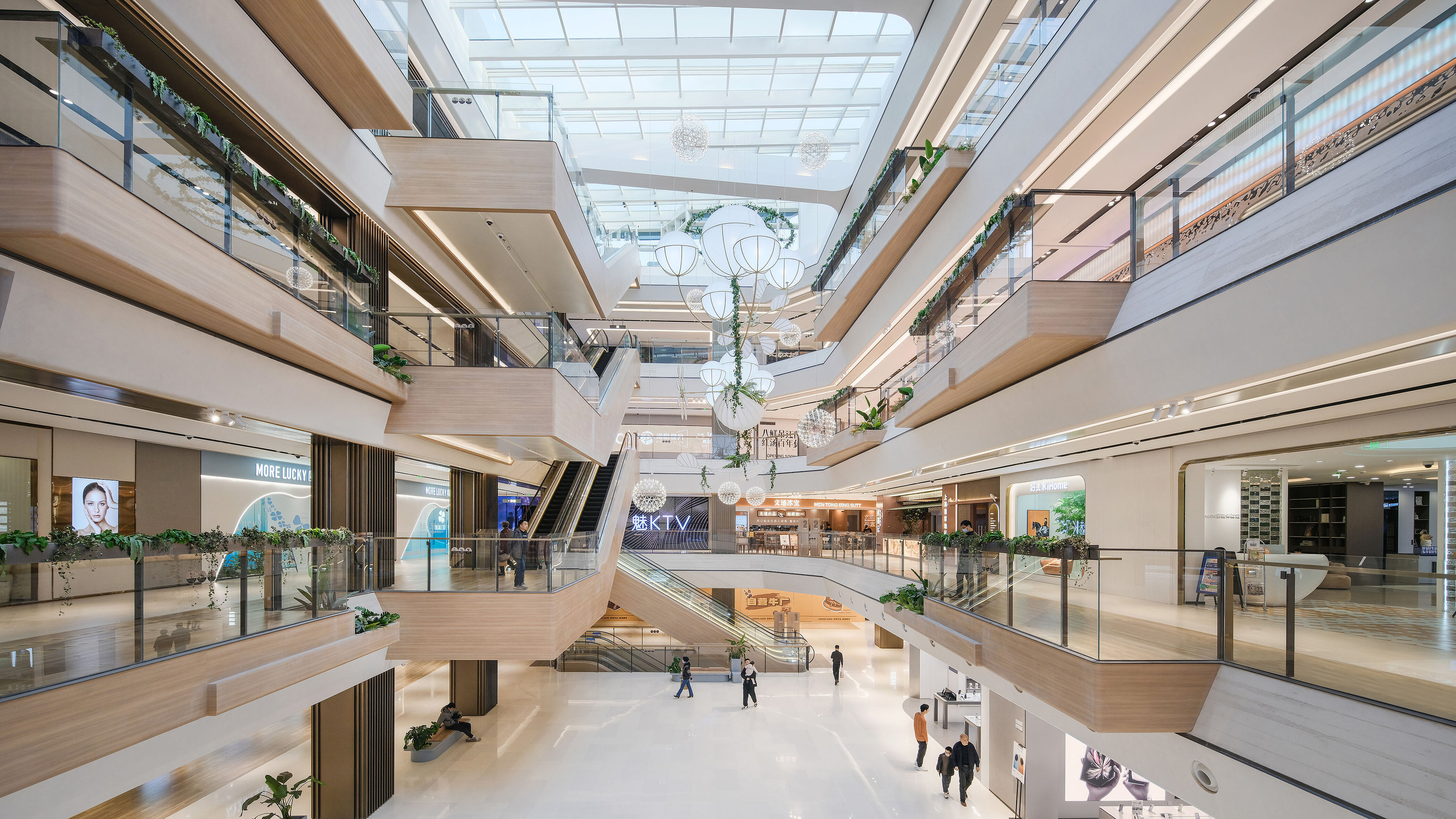 Blick ins Innere eines in hellen Farben gehaltenen Shopping-Centers mit architektonischen Besonderheiten, heller Holzverkleidung und Sonnenlicht, das durch das Glasdach fällt.