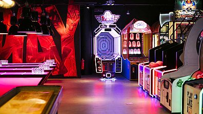 Auf dem Bild sind verschiedene Spieleautomaten im Neon-Licht zu sehen.