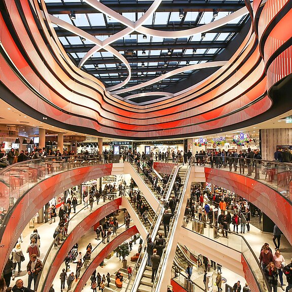 Im Inneren eines Einkaufszentrums mit vielen Menschen und einem rot-beleuchteter Innenausstattung.