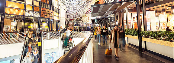 Bunte und grelle Farben inmitten eines Shopping-Centers mit vielen Besucherinnen und Besuchern