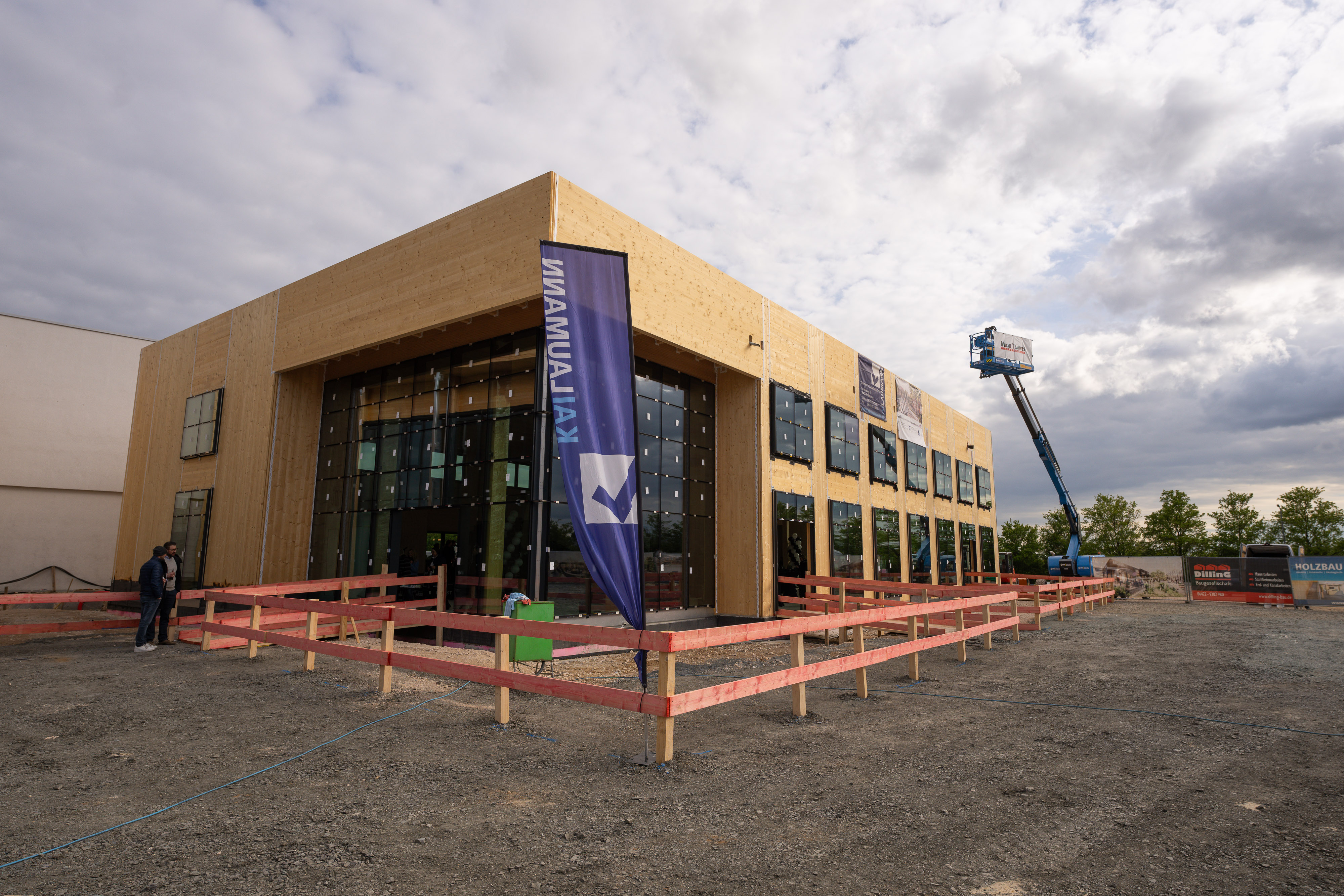 Auf dem Bild ist ein großes Gebäude zu sehen, mit Baukran und Baustellenzaun.